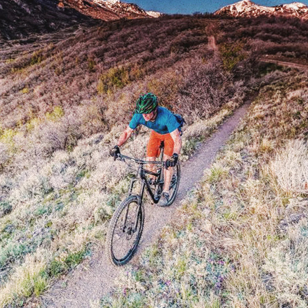 mountain biker wearing a blue shirt and orange shorts, riding on a hillside with scenic view