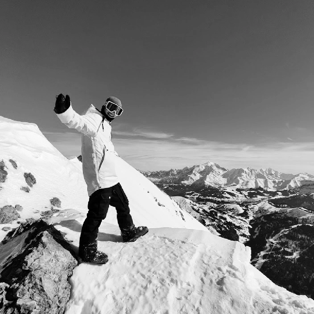 man wearing a ski jacket smiling with a snow covered mountains at the back