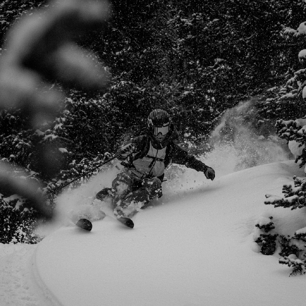 A man speeds downhill on a sled, surrounded by snow-covered trees