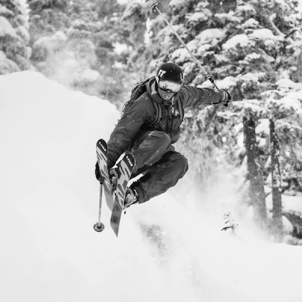 A man jumps mid-air amidst a cloud of powdery snow, on a steep hil