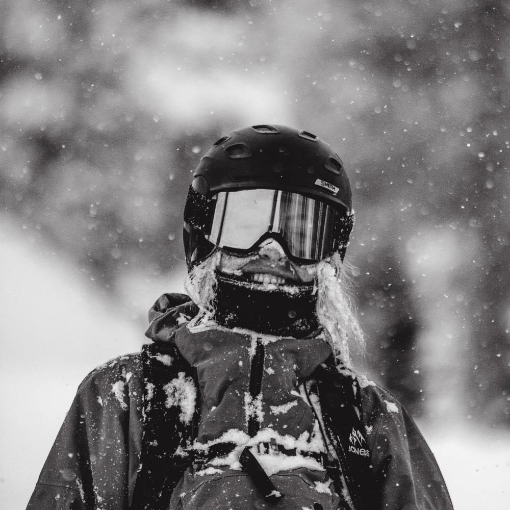 Person standing with snow on their ski jacket, wearing goggles and a warm ski jacket.